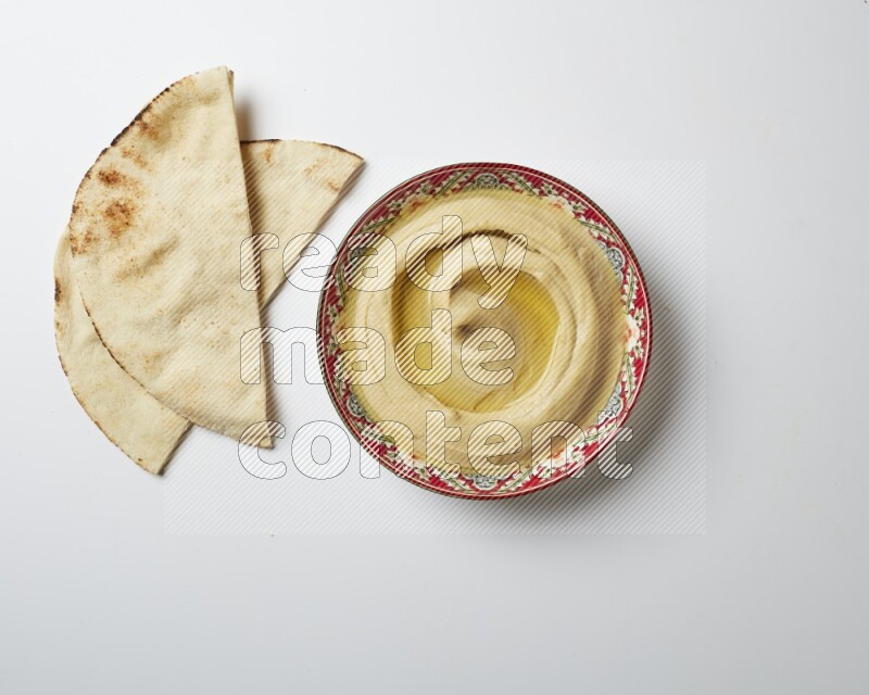 Hummus in a red plate with patterns garnished with olive oil on a white background
