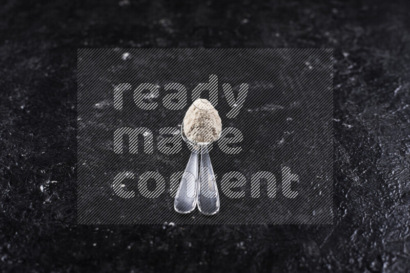 Two metal spoons full of onion powder on black background