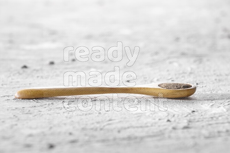 A wooden spoon full of black pepper powder on a textured white flooring