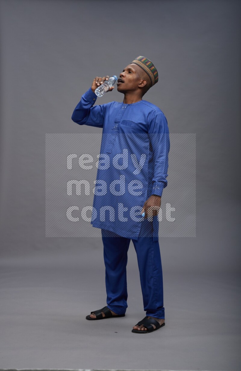 Man wearing Nigerian outfit standing drinking water on gray background