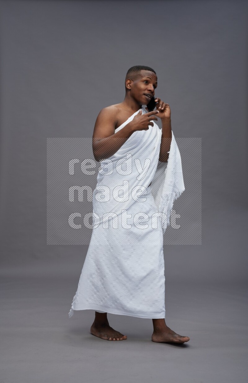 A man wearing Ehram Standing talking on phone on gray background