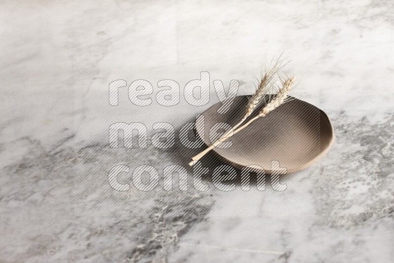 Wheat stalks on multicolored pottery plate on grey marble background