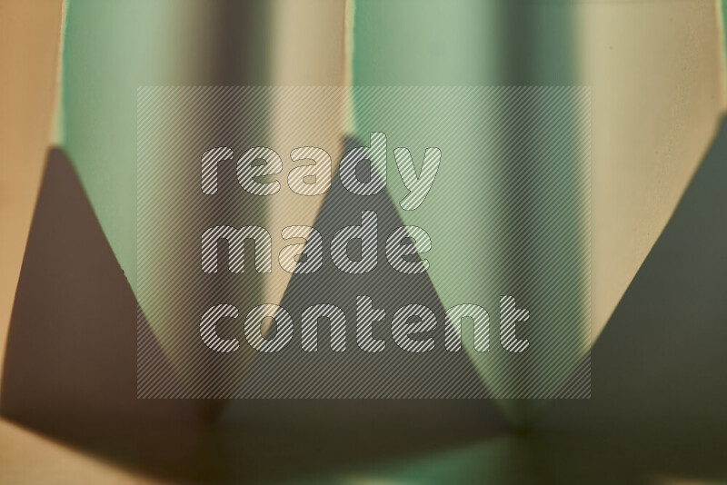 A close-up abstract image showing sharp geometric paper folds in green gradients and warm tones