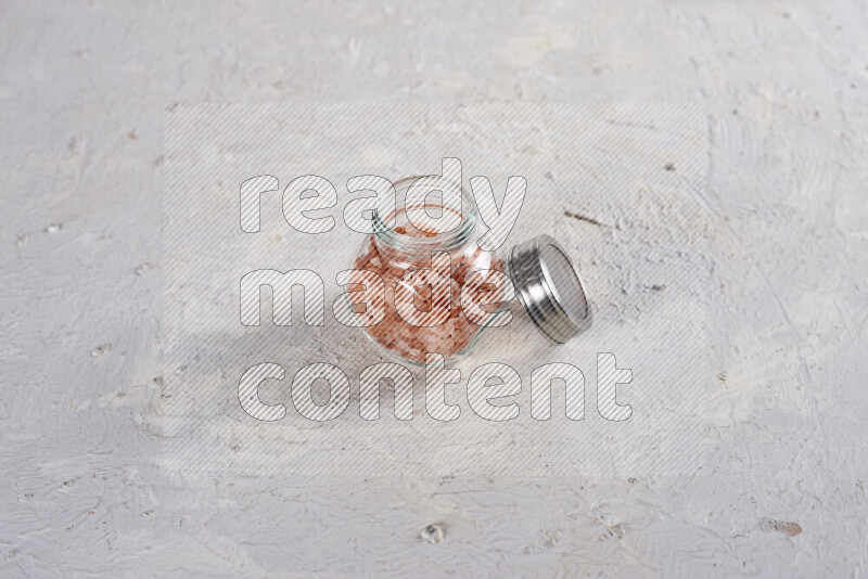 A glass jar full of coarse himalayan salt crystals on white background