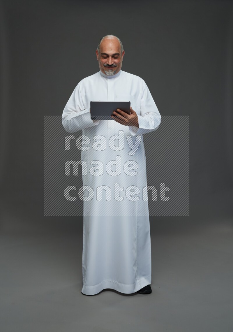 Saudi man without shomag Standing working on tablet on gray background