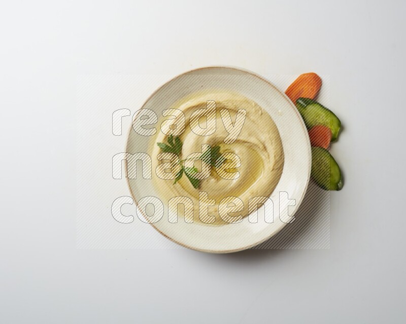 Hummus in a pottry plate garnished with parsley on a white back ground