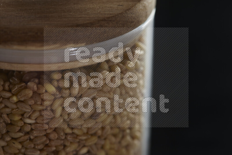 Hulled wheat in a glass jar on black background