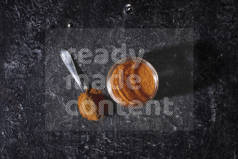 A glass jar full of ground paprika powder on black background
