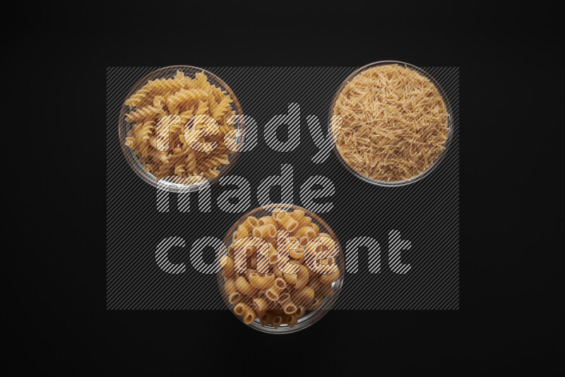 Different pasta types in glass bowls on black background