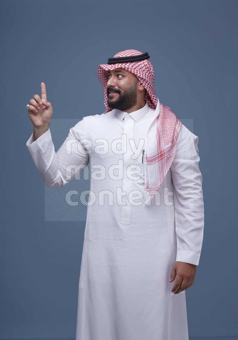 A man pointing on blue background wearing Saudi Thob with Shomag