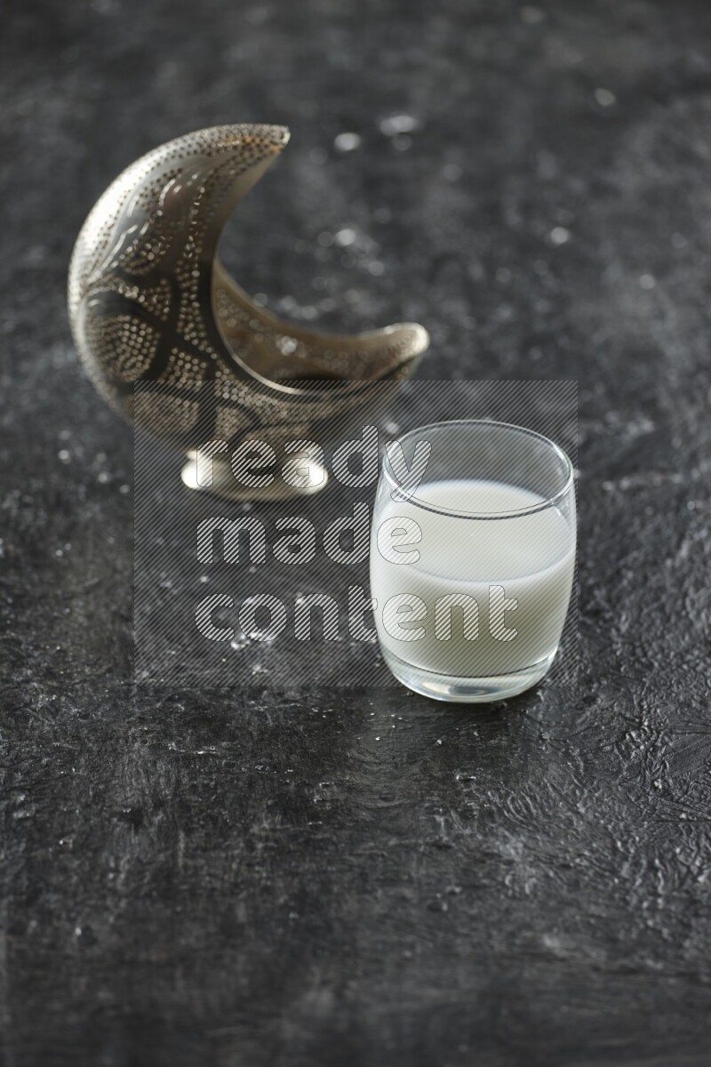 A silver lantern with different drinks, dates, nuts, prayer beads and quran on textured black background