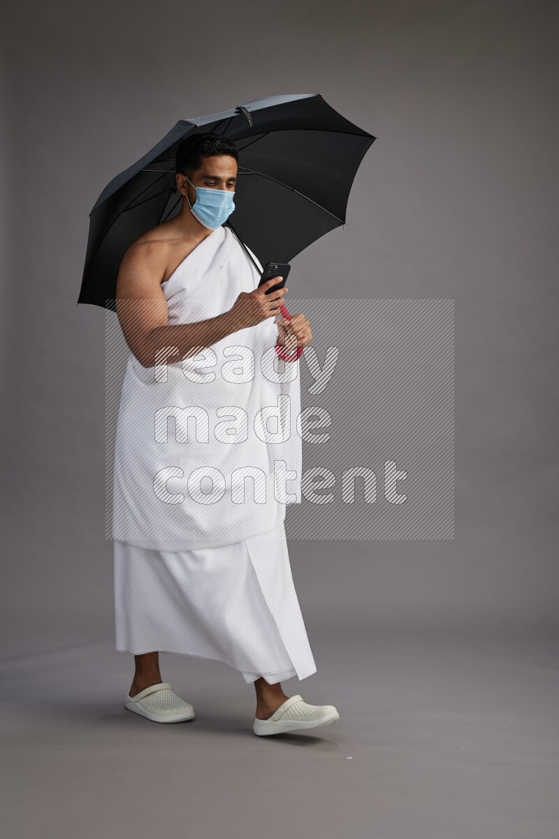 A man wearing Ehram and mask Standing holding umbrella on gray background on gray background