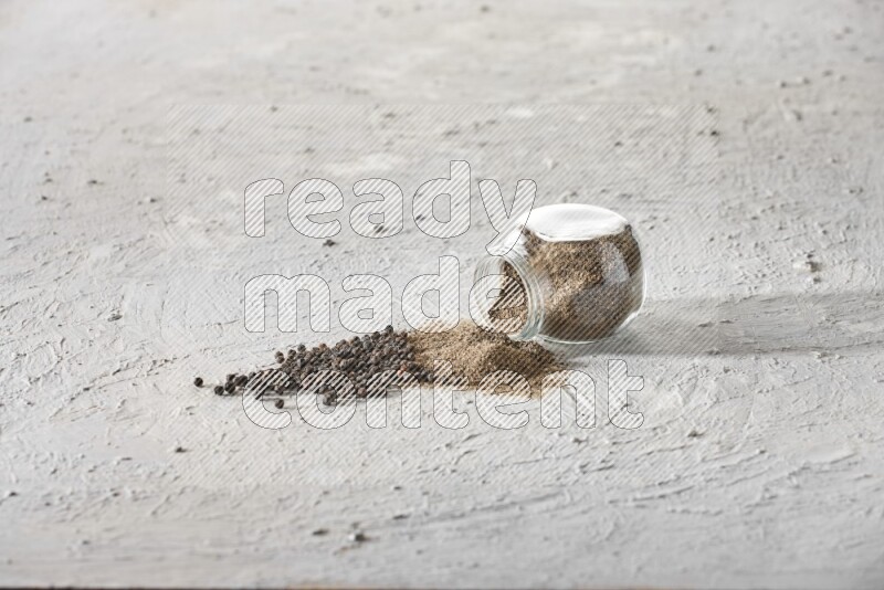 Flipped glass spice jar full of black pepper powder and paper beads beside it on a textured white flooring