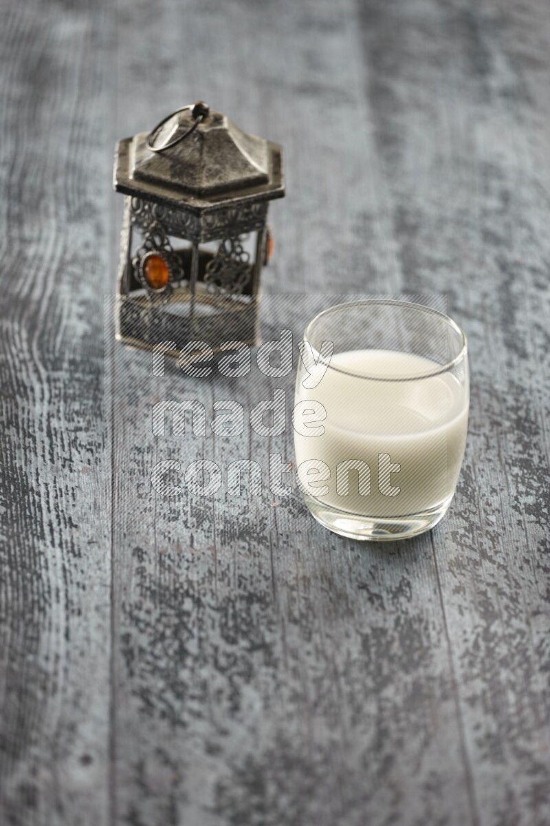 فانوس فضي مع مشروبات مختلفة وتمر ومكسرات وسبحة صلاة وقرآن على خلفية خشبية رمادية