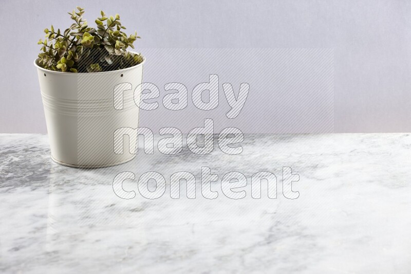 Green artificial plant in white pot on light grey marble background
