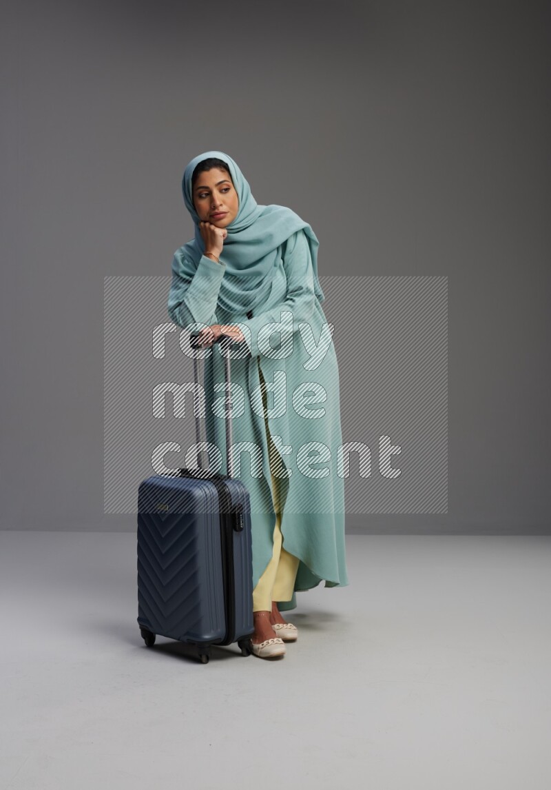 Saudi Woman wearing Abaya standing holding Travel bag on Gray background