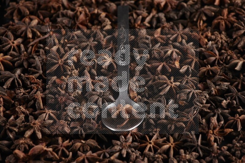 Star Anise in a metal spoon on more stars anise filling the frame on black flooring
