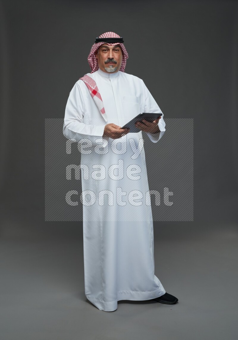 Saudi man with shomag Standing working on tablet on gray background