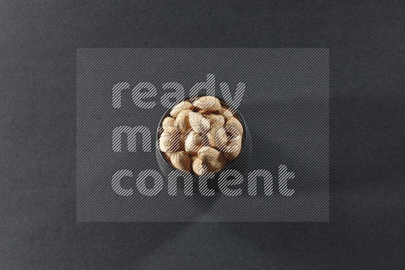 A black pottery bowl full of almonds on a black background in different angles