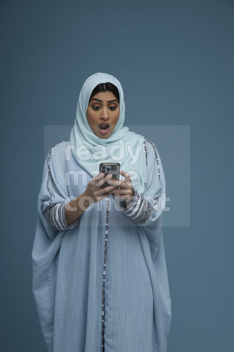 A Saudi woman Texting in a blue background wearing a blue Abaya with hijab