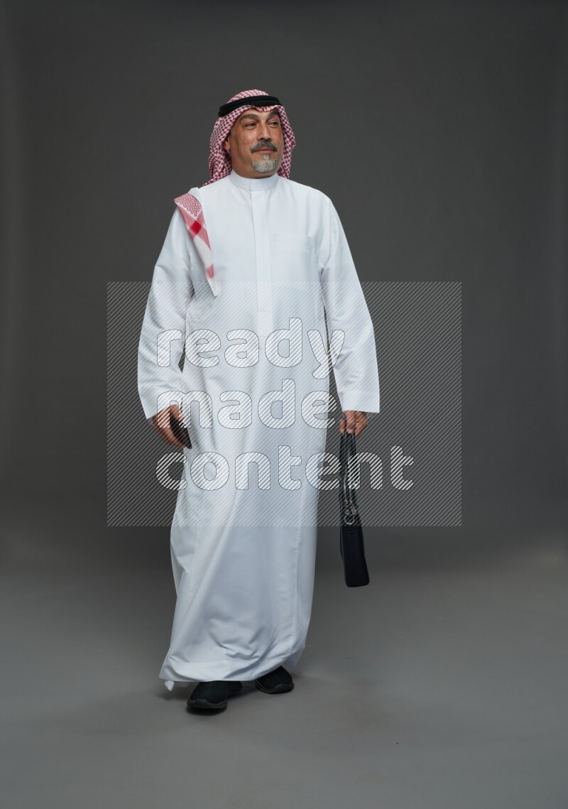 Saudi man with shomag Standing holding bag and phone on gray background