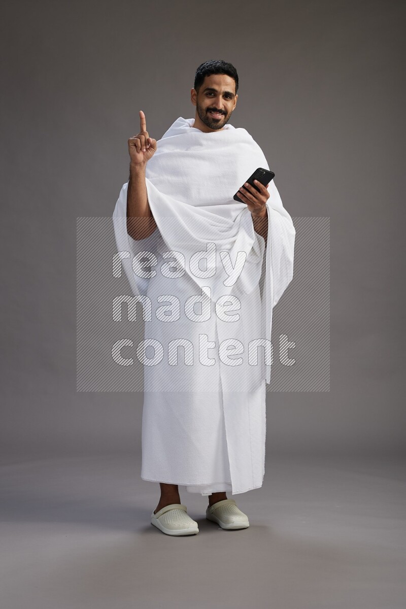 A man wearing Ehram Standing texting on phone on gray background