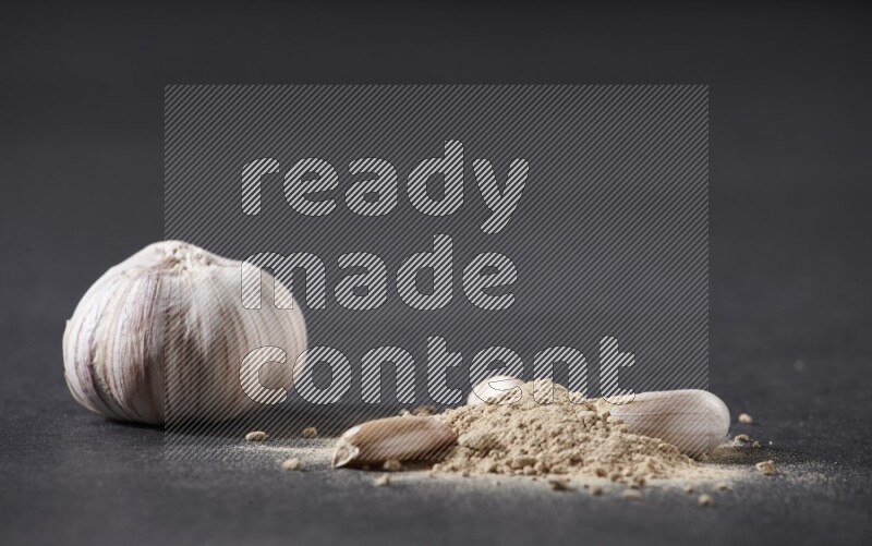 A small pile of garlic powder with some of cloves and a whole garlic bulb on a black flooring