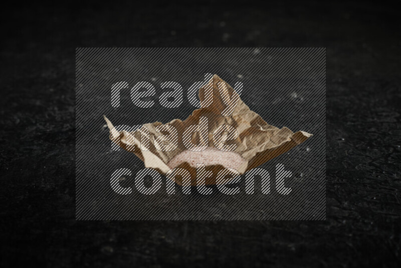 A crumpled piece of paper full of pink himalayan salt on black background