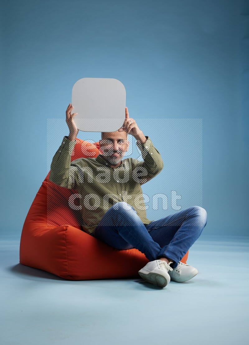 A man sitting on a orange beanbag and holding social media sign