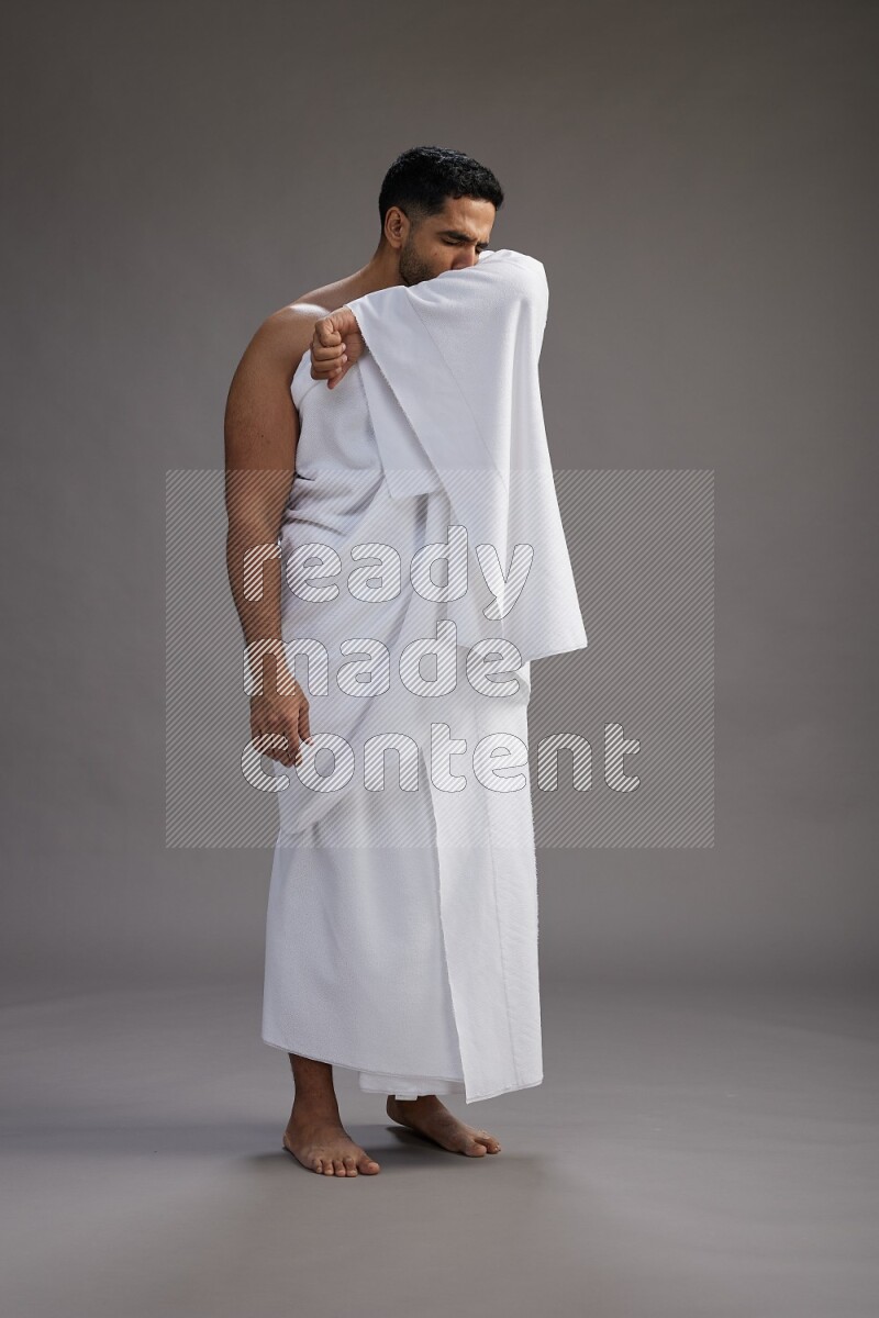 A man wearing Ehram standing showing how to sneeze on gray background