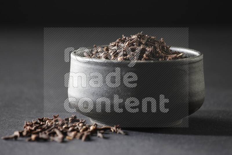 A black pottery bowl full of cloves on a black flooring