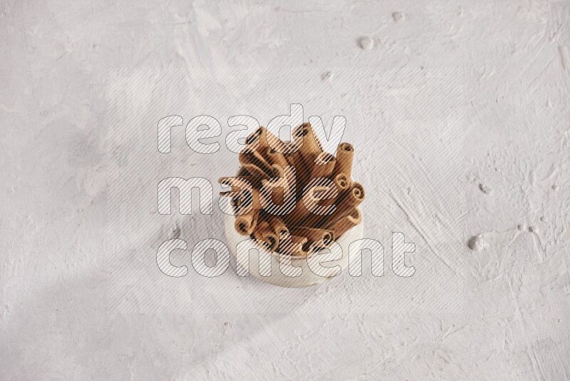 Cinnamon sticks in a beige bowl and more sticks beside it on white background