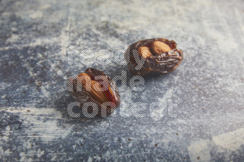 two almond stuffed madjoul dates on a rustic blue background