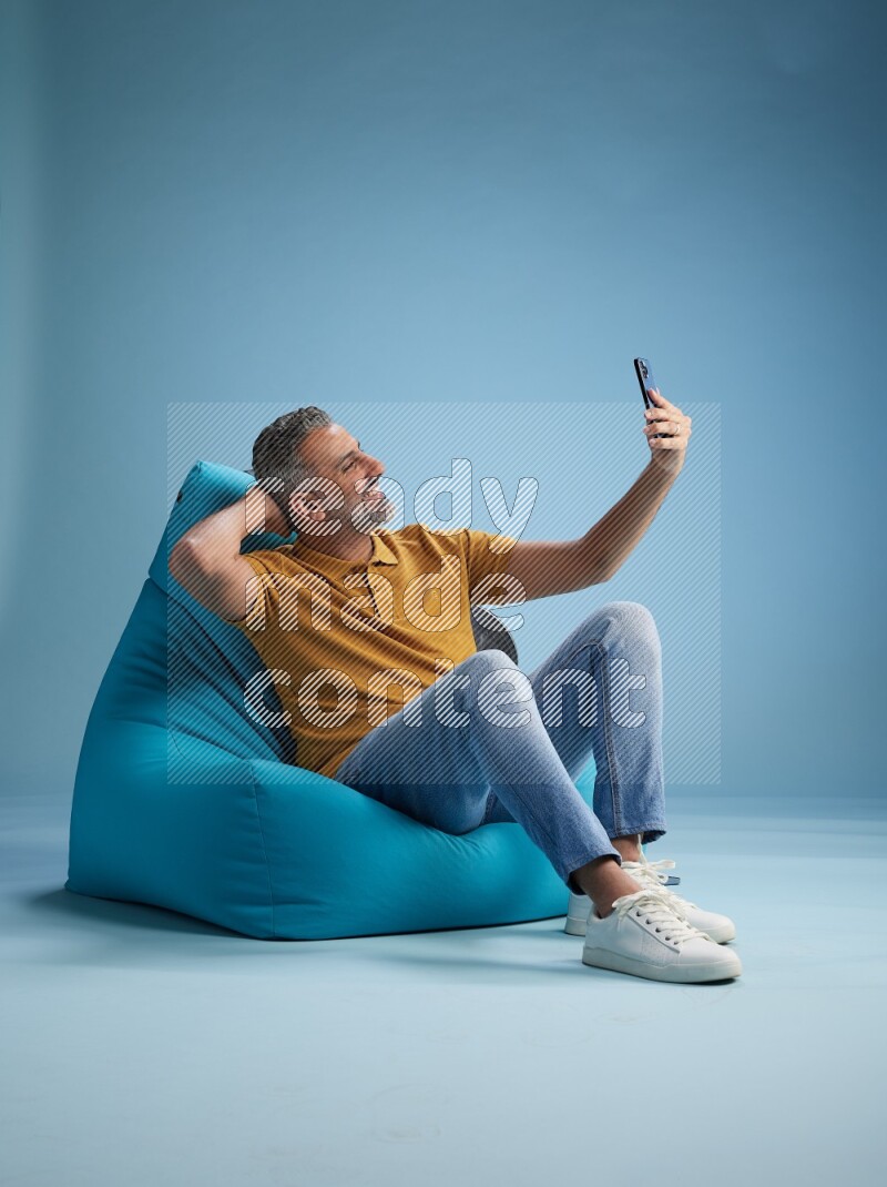 A man sitting on a blue beanbag and taking selfie