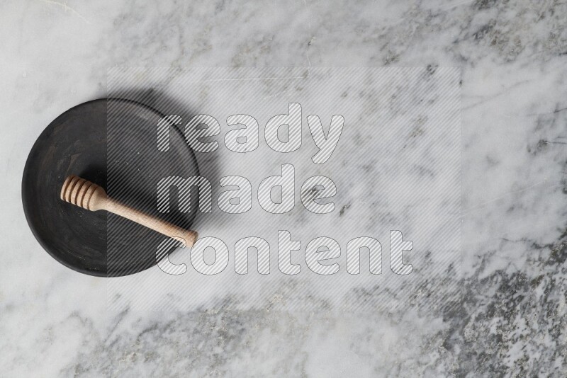 Black pottery plate with wooden honey dipper in it on grey marble background