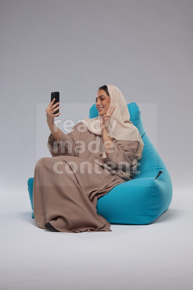 A Saudi woman sitting on a blue beanbag and taking selfie