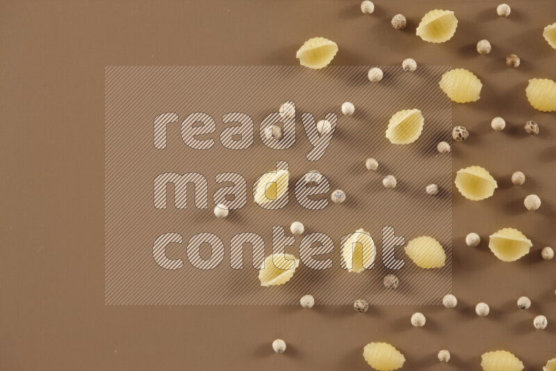 Raw pasta with different ingredients such as cherry tomatoes, garlic, onions, red chilis, black pepper, white pepper, bay laurel leaves, rosemary and cardamom on beige background