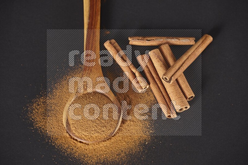 Cinnamon powder in a spoon ladle and spreaded on the floor beside it cinnamon sticks on the floor on black background in different angles
