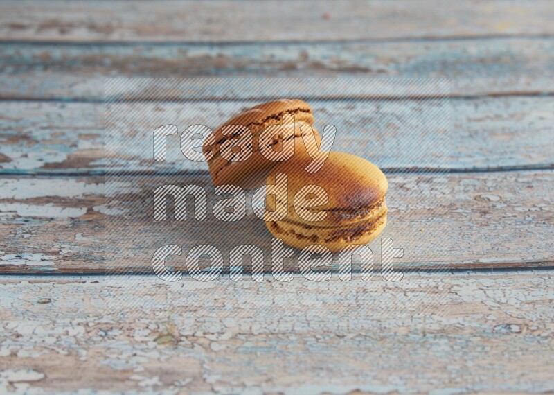 45º Shot of of two assorted Brown Irish Cream, and Yellow Crème Brulée macarons on light blue background