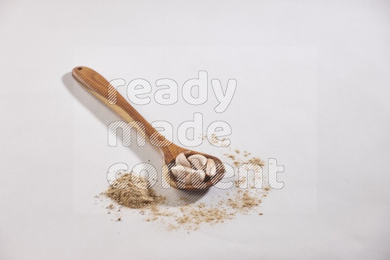 A wooden ladle full of garlic cloves with sprinkled powder on a white flooring