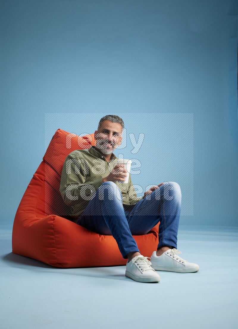 A man sitting on an orange beanbag and drinking coffee