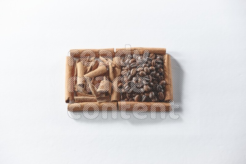 مربعان من أعواد القرفة ممتلئان بحبوب القهوة وقطع من القرفة علي خلفية بيضاء