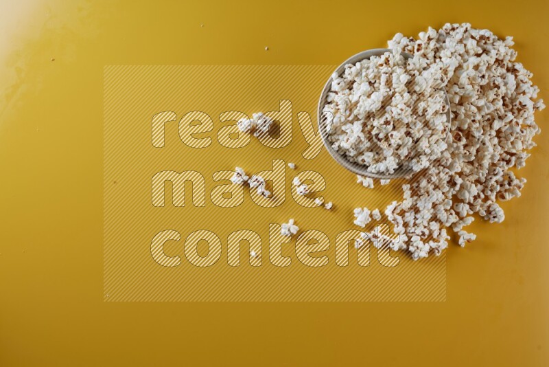 A white pottery bowl full of popcorn with popcorn beside it on a yellow background in different angles