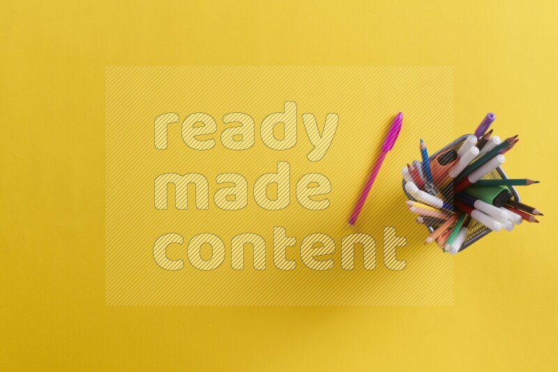 Pens, pencils and school supplies in a metal pen holder on yellow background