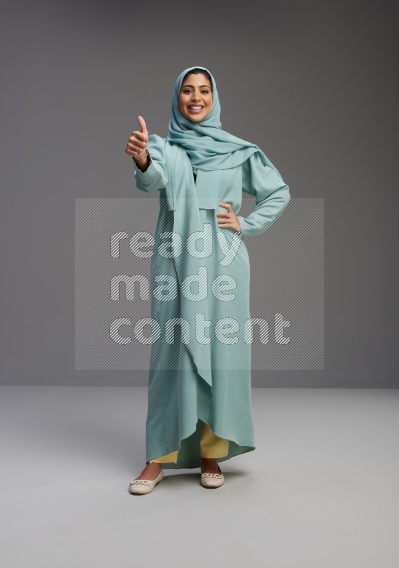 Saudi Woman wearing Abaya standing interacting with the camera on Gray background