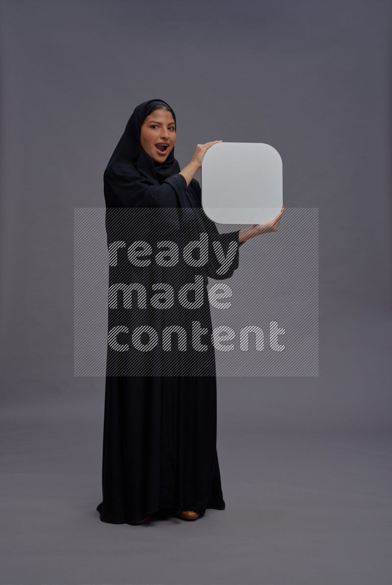 Saudi woman wearing Abaya standing holding social media sign on gray background