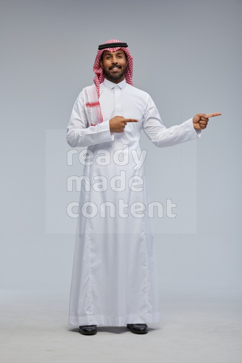 Saudi man Wearing Thob and shomag standing interacting with the camera on Gray background