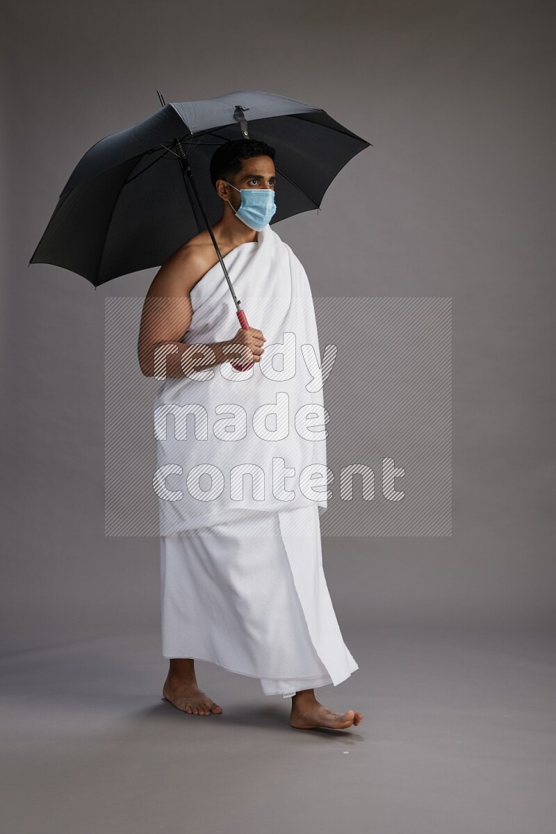 A man wearing Ehram and mask Standing holding umbrella on gray background on gray background