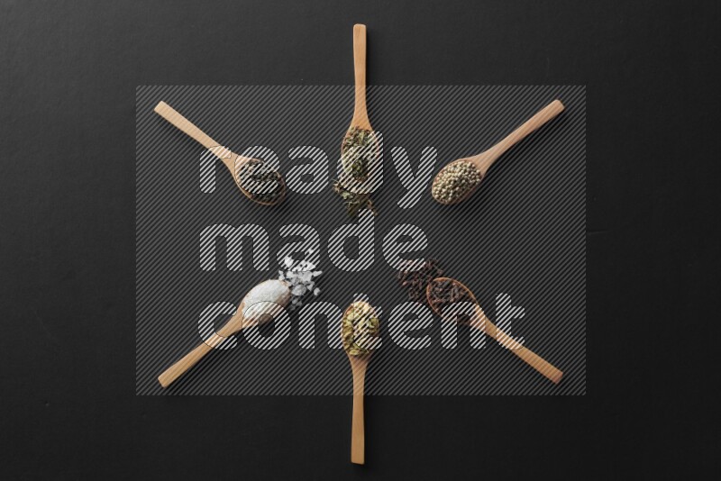 wooden spoons filled with white peppers, cloves, cardamom, salt, black peppers and basil on black flooring and shaped like a clock