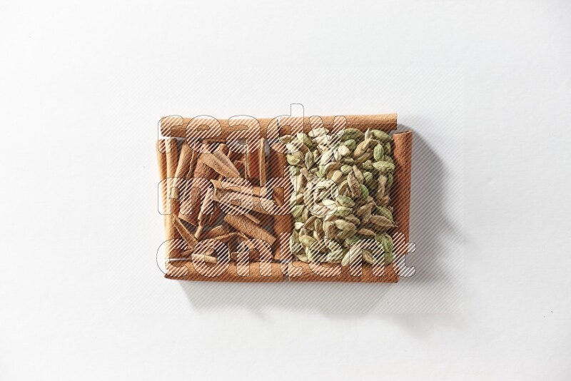 مربعان من أعواد القرفة ممتلئان بقطع من القرفة وحبوب الهيل علي خلفية بيضاء